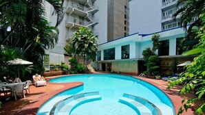 A swimming pool surrounded by lush greenery and a multi-story building with balconies. - Manhattan Bangkok (Bangkok)