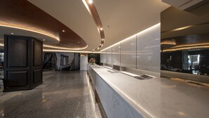 A modern hotel lobby with a long reception desk, a large mural of a bridge, and a curved ceiling design. - Manhattan Bangkok (Bangkok)
