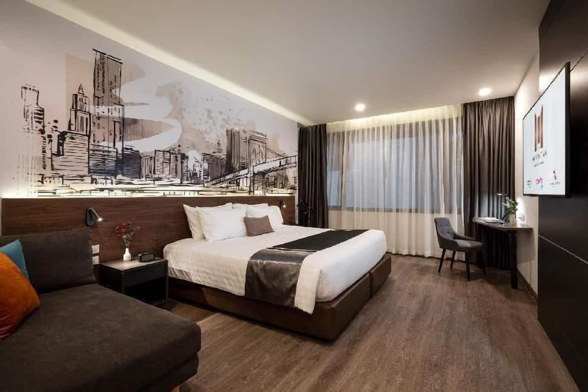 Una habitación de hotel con una cama grande, un sofá, un escritorio y un mural con vistas a la ciudad.
