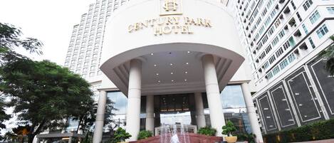 L'entrée de l'hôtel Century Park se distingue par son design moderne, avec un hall d'entrée imposant, un élément décoratif aquatique et un jardin bien entretenu.