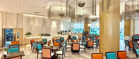 A spacious hotel lobby with multiple dining areas, a central bar, and a view of the outdoors.