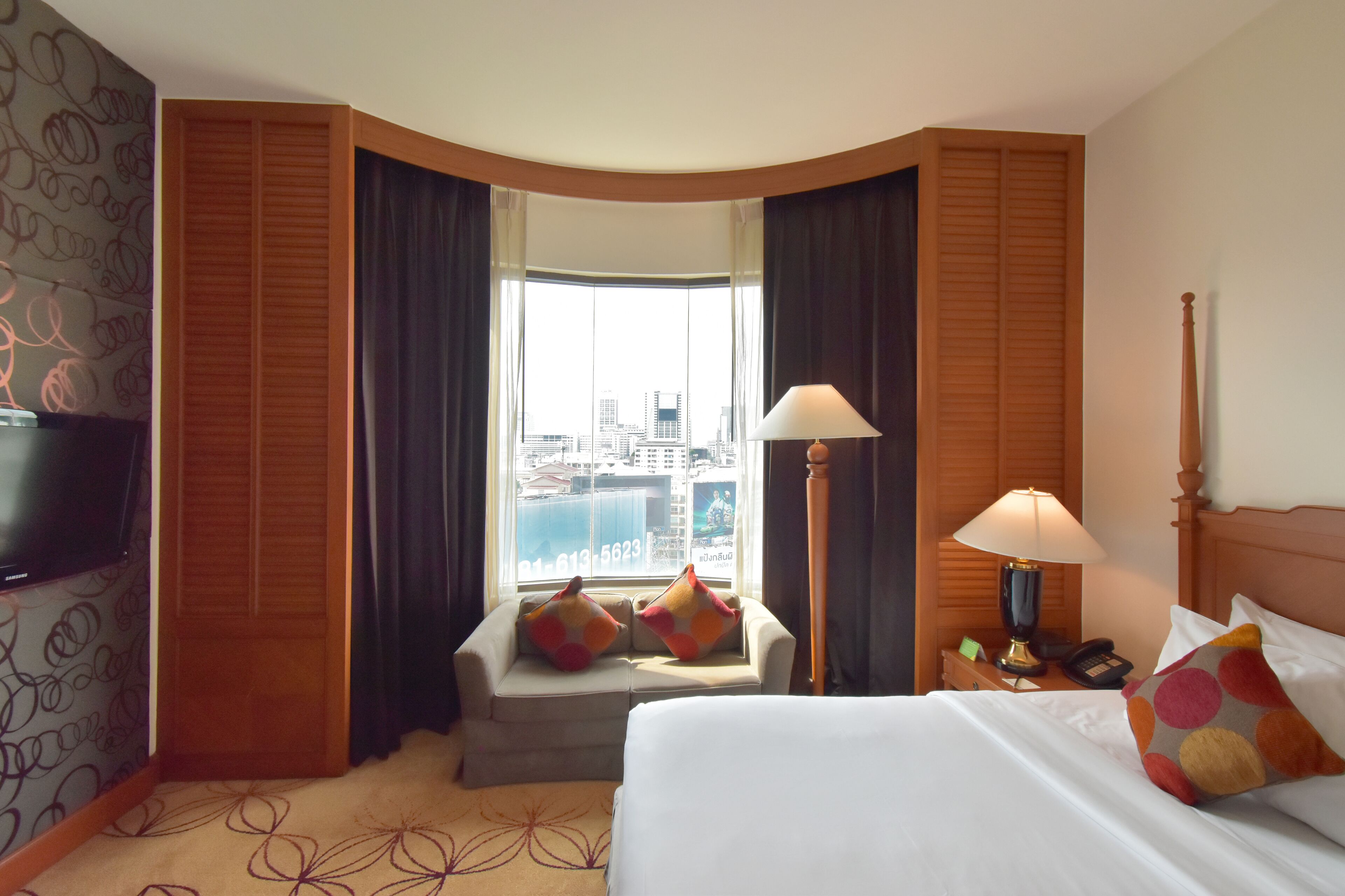 Habitación de hotel con cama, televisor, escritorio con lámpara y ventana con vista a la ciudad.