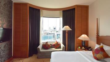 Habitación de hotel con cama, televisor, escritorio con lámpara y ventana con vista a la ciudad.