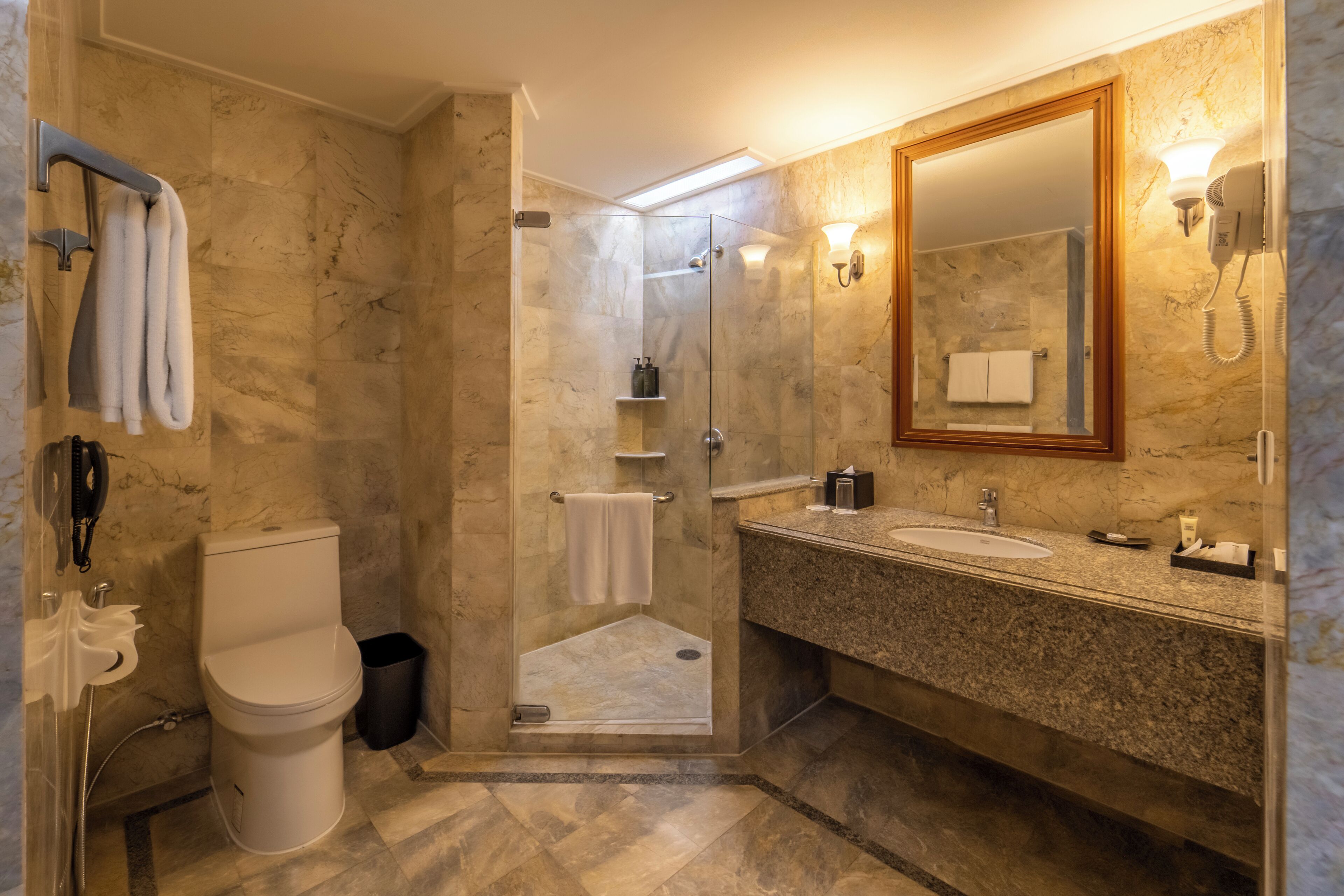 Un baño moderno con ducha de vidrio, inodoro y lavamanos con encimera de mármol.