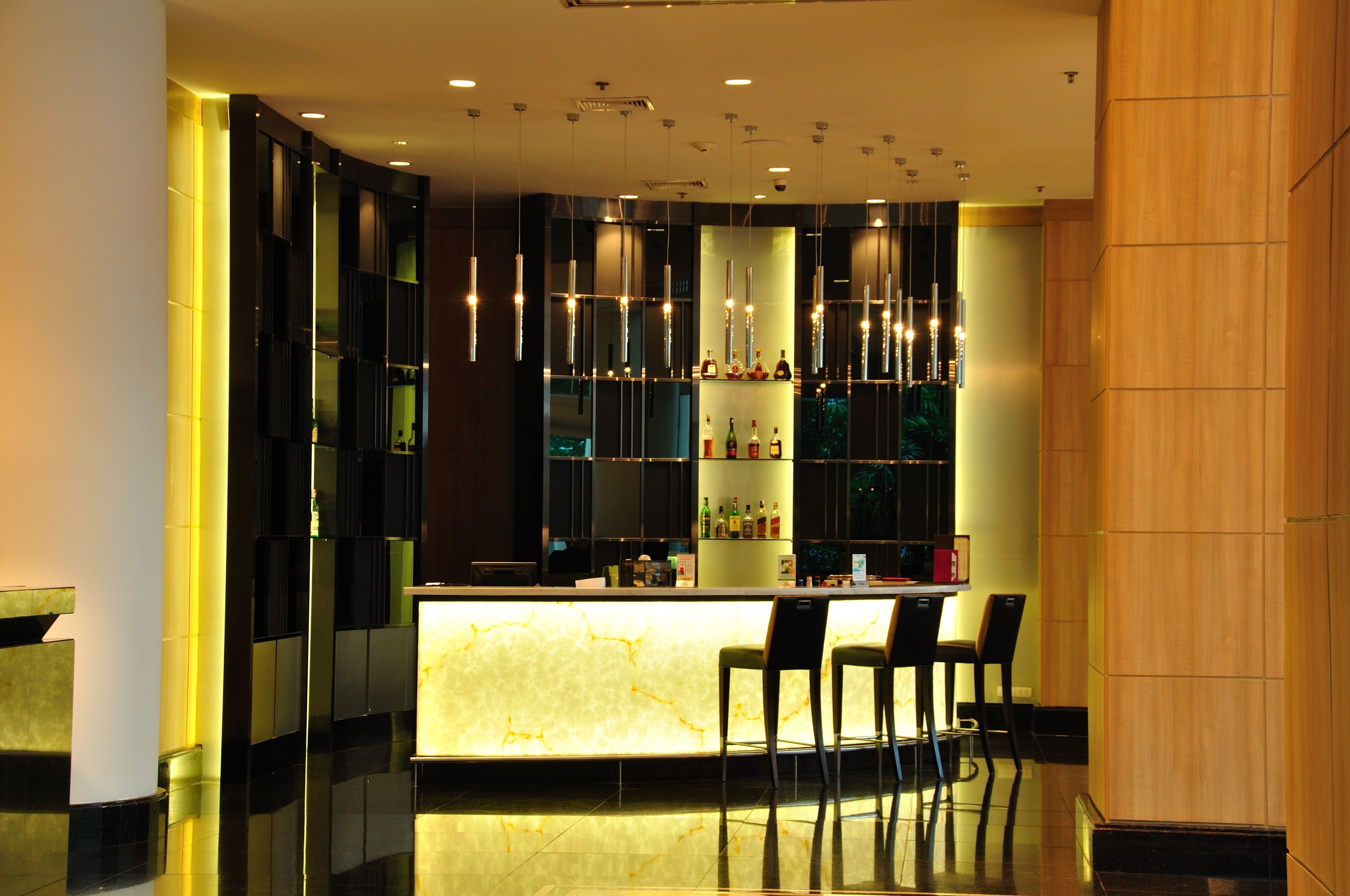 A modern bar area with a marble countertop, hanging pendant lights, and a selection of bottles on shelves.