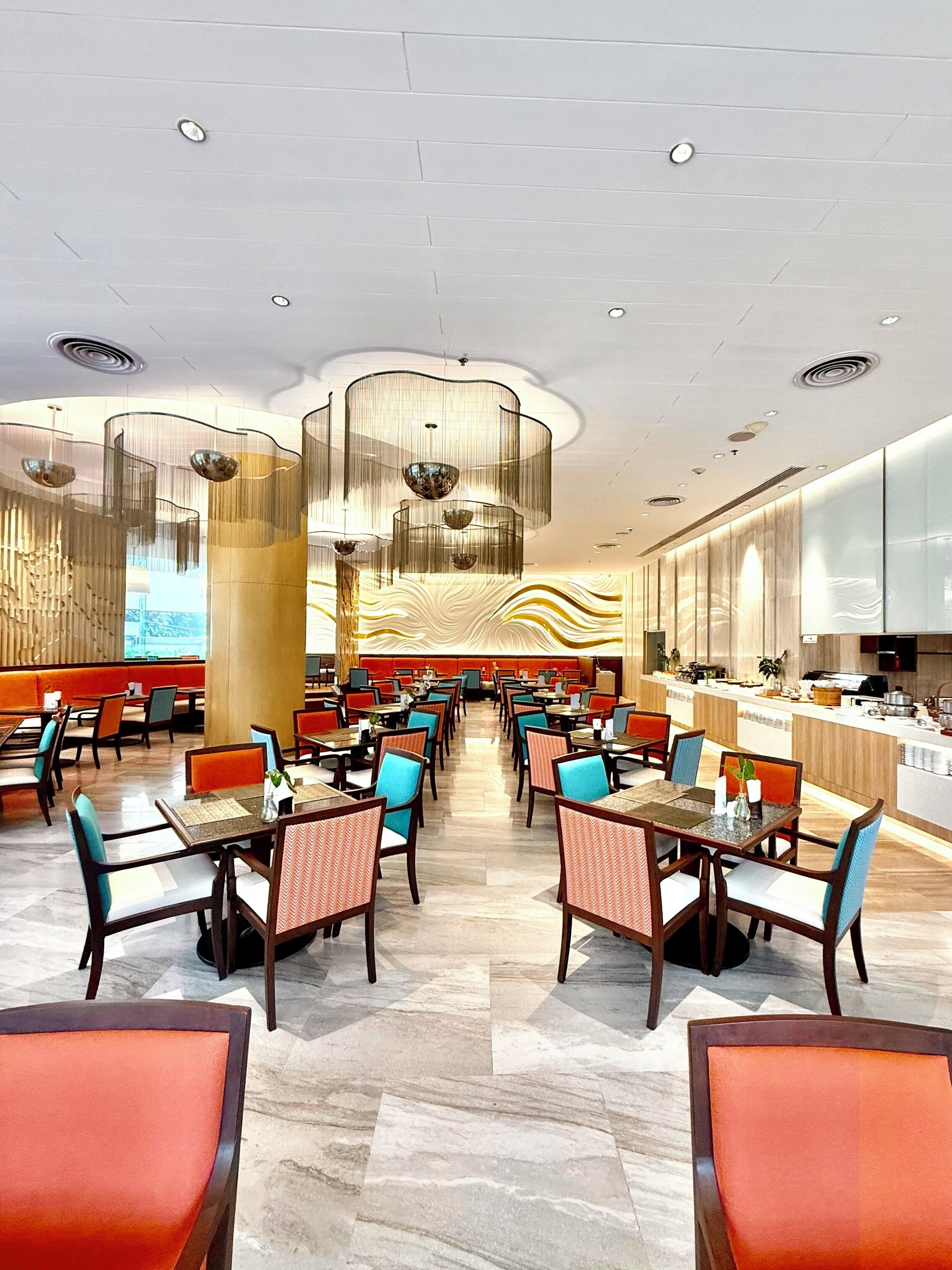Un restaurante moderno con techos altos, luminarias contemporáneas y una zona central de asientos con una barra alargada.