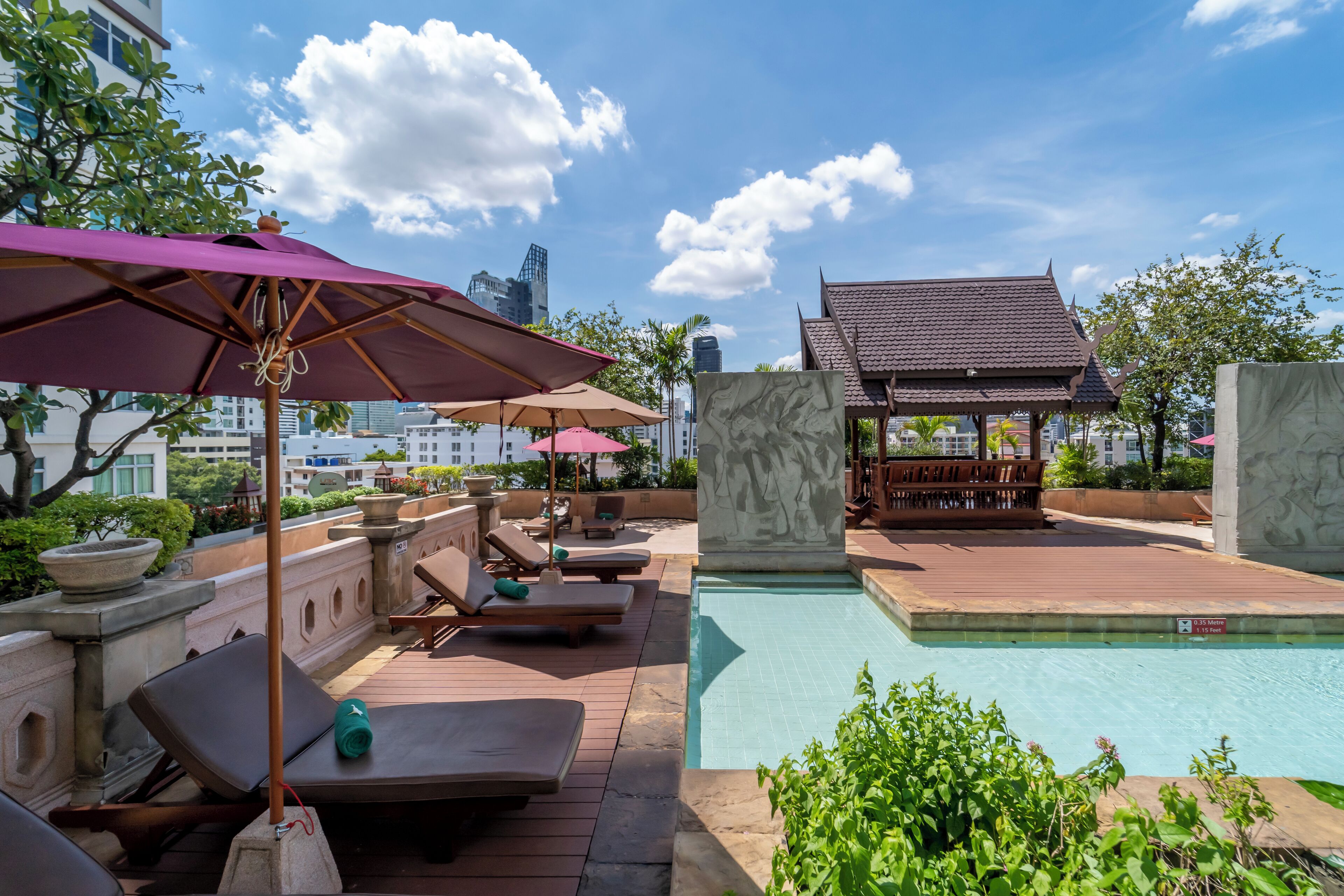 Un espace piscine sur le toit, avec des chaises longues et des parasols, un petit pavillon et une vue sur le panorama urbain.