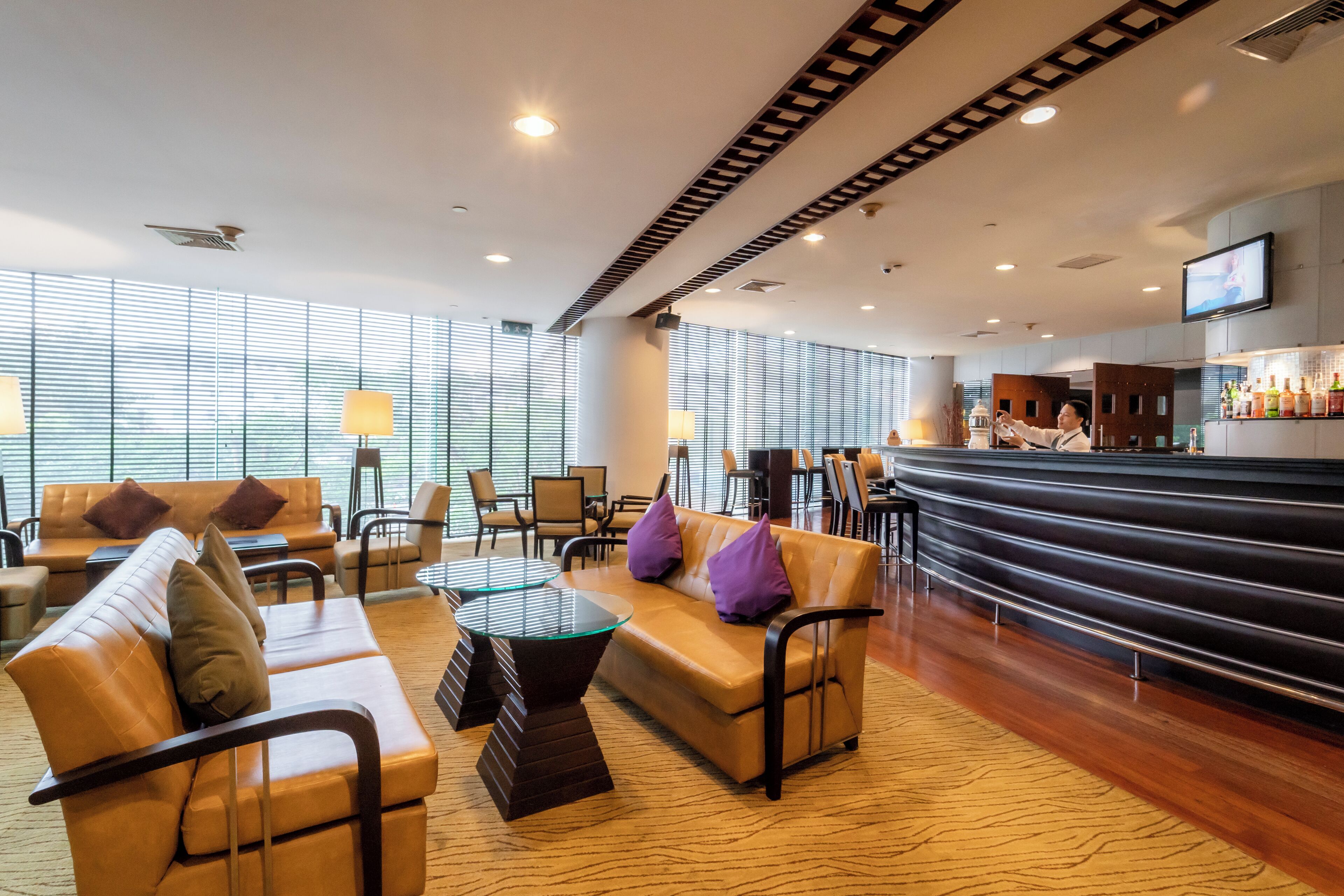 A modern hotel lobby with leather sofas, a glass coffee table, and a bar area with bottles.
