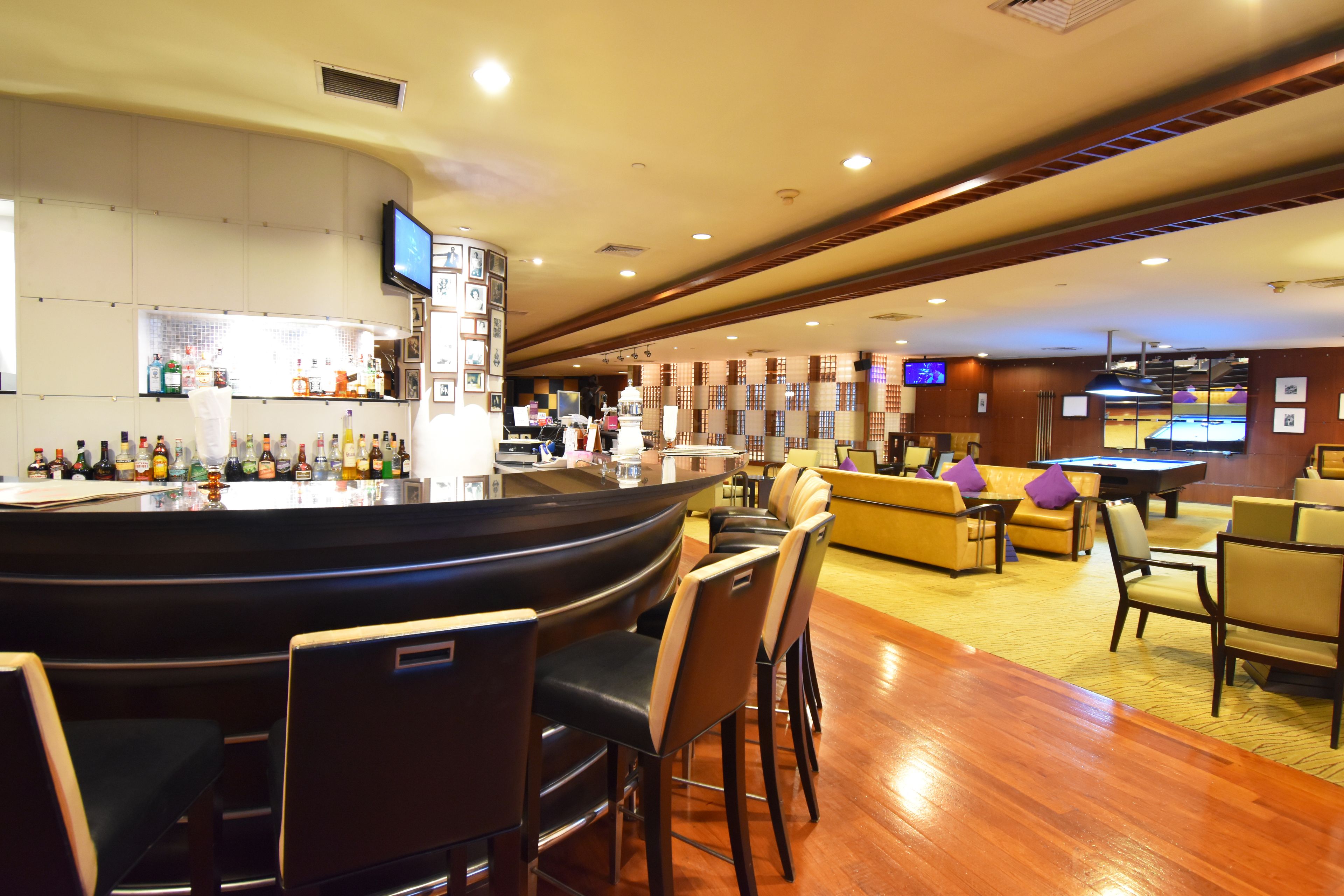 A bar area with a curved counter, multiple bar stools, and a television mounted on the wall.