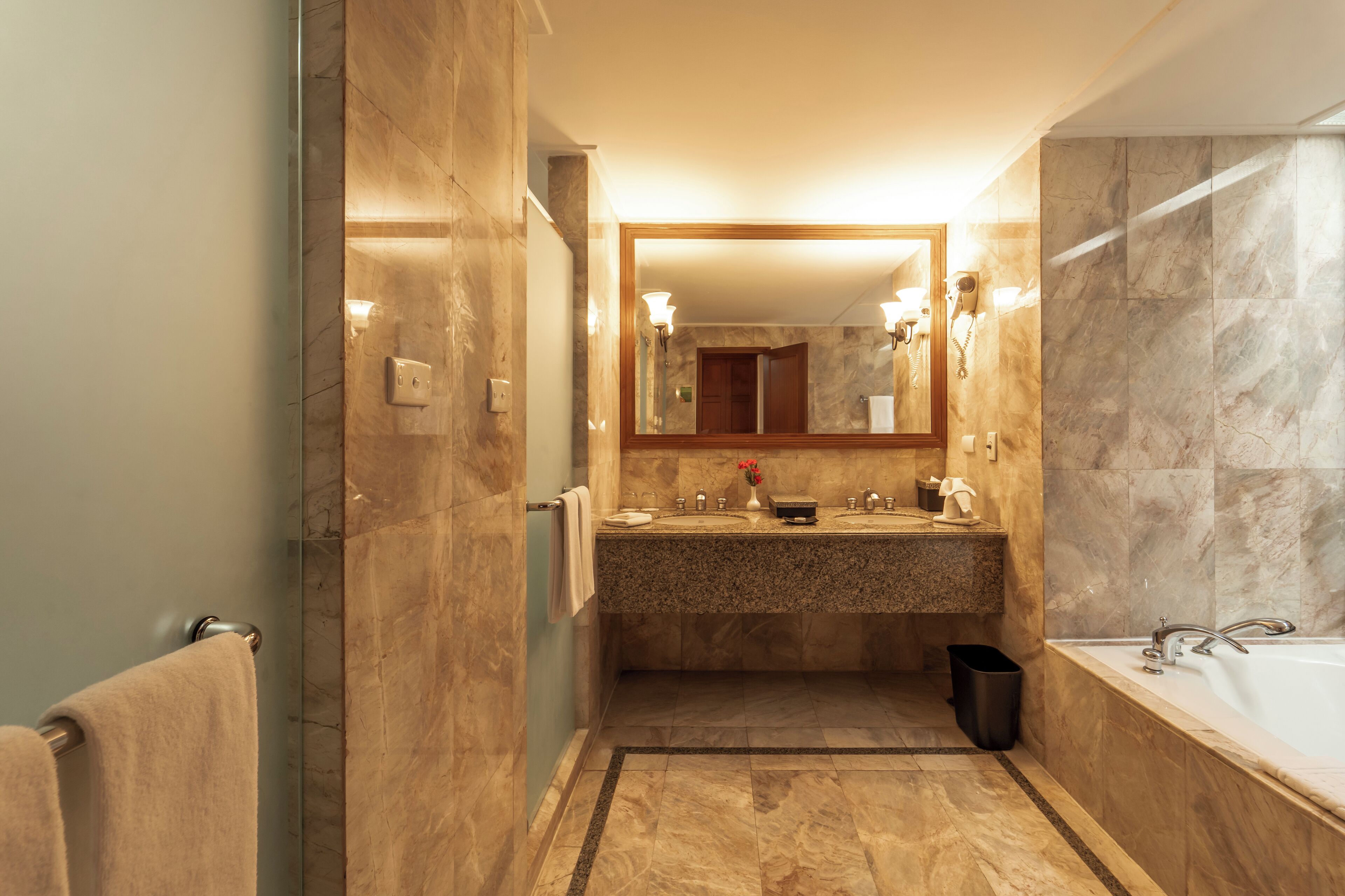 Un baño moderno con suelo de mármol, tocador doble, espejo grande y bañera.