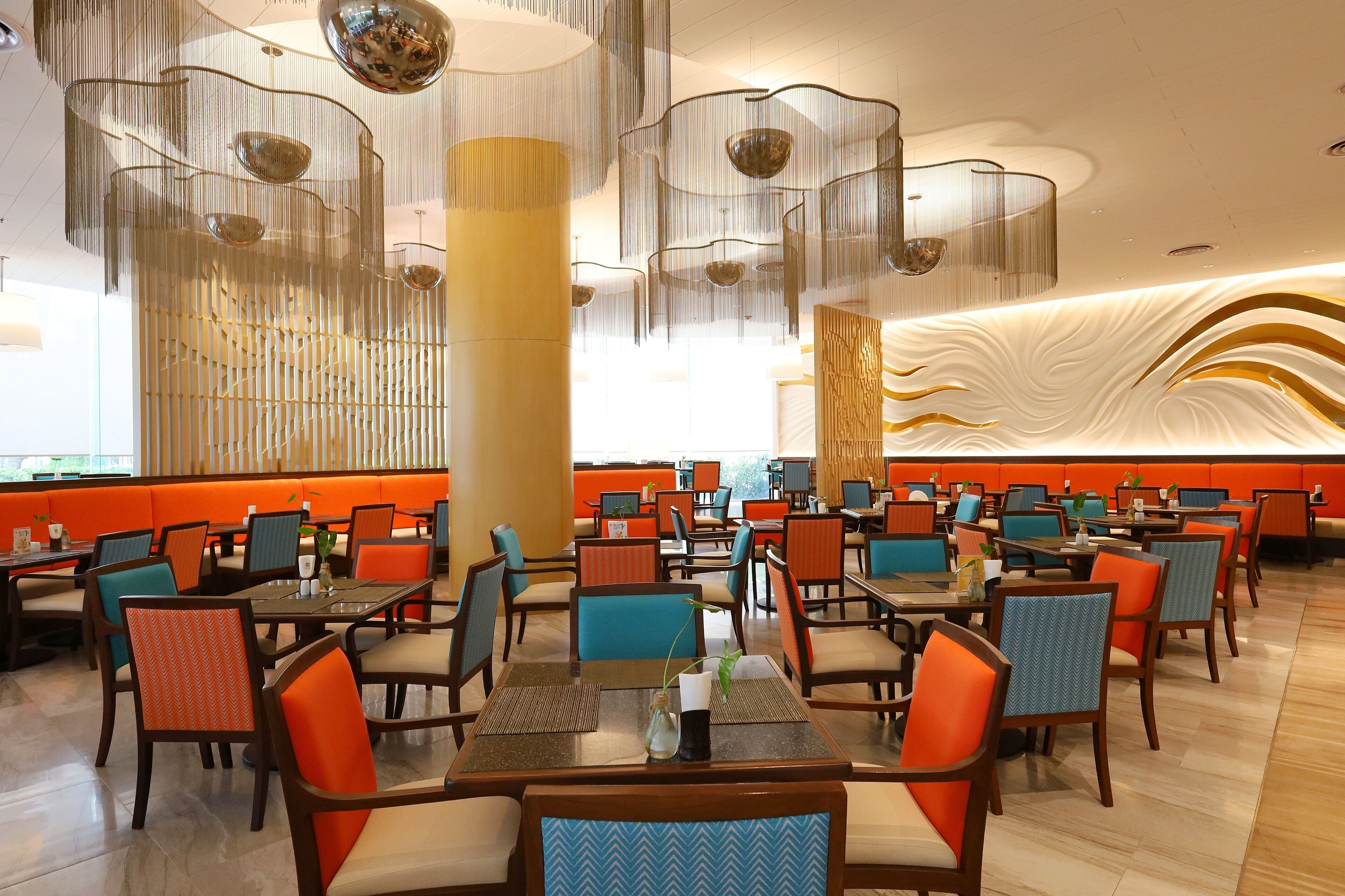 A spacious dining area with multiple tables and chairs, a large pillar, and a decorative wall with a wave-like pattern.