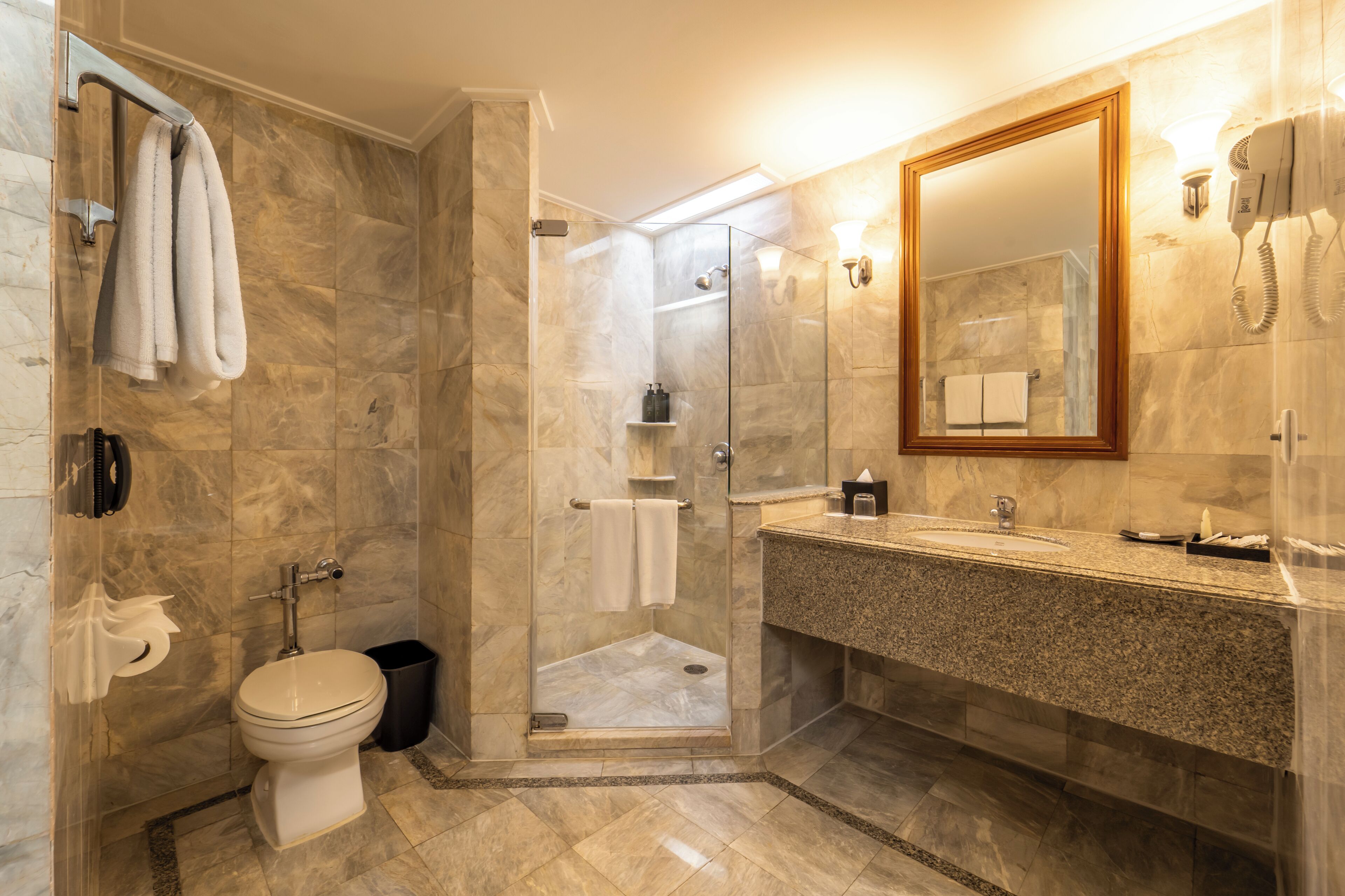 Une salle de bain moderne dotée d’une douche à parois de verre, d’un sol carrelé en marbre, d’un lavabo avec un plan de travail en granit et d’un grand miroir.