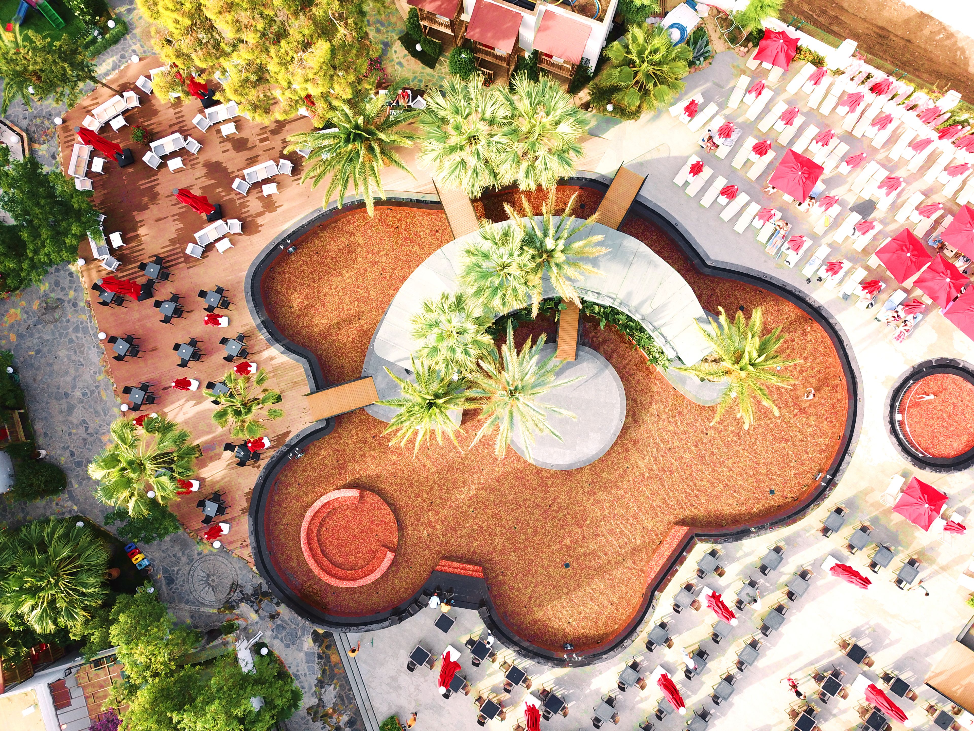 An aerial view of a resort with multiple lounge areas, palm trees, and a central circular water feature.