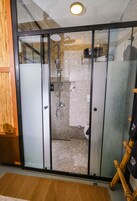 A modern bathroom with a glass shower enclosure, a wooden bench, and a towel rack.