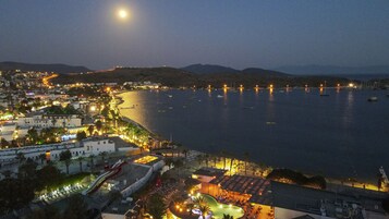 Un pueblo costero de noche con playa, barcos y un paseo marítimo iluminado.