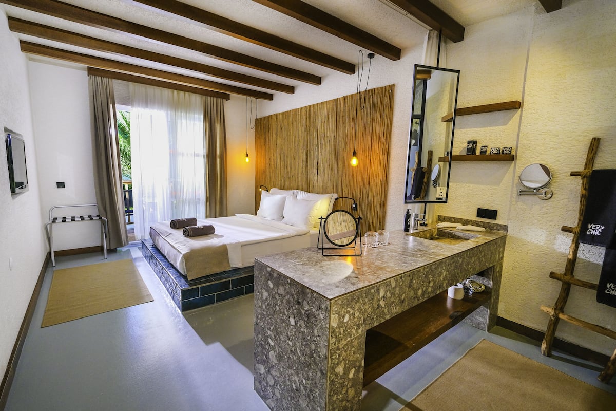 Une chambre d’hôtel avec un lit, une salle de bain comprenant un lavabo et un miroir, et un plafond en bois.