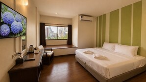 A hotel room with a bed, a desk with a chair, a window with a view of buildings, and an air conditioning unit.