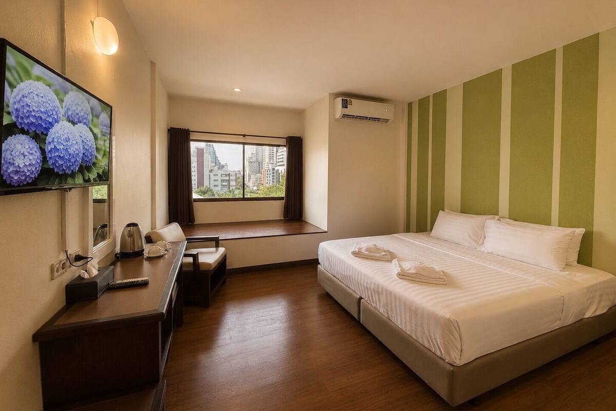 Habitación de hotel con cama, escritorio con silla, ventana con vista a edificios y un equipo de aire acondicionado.