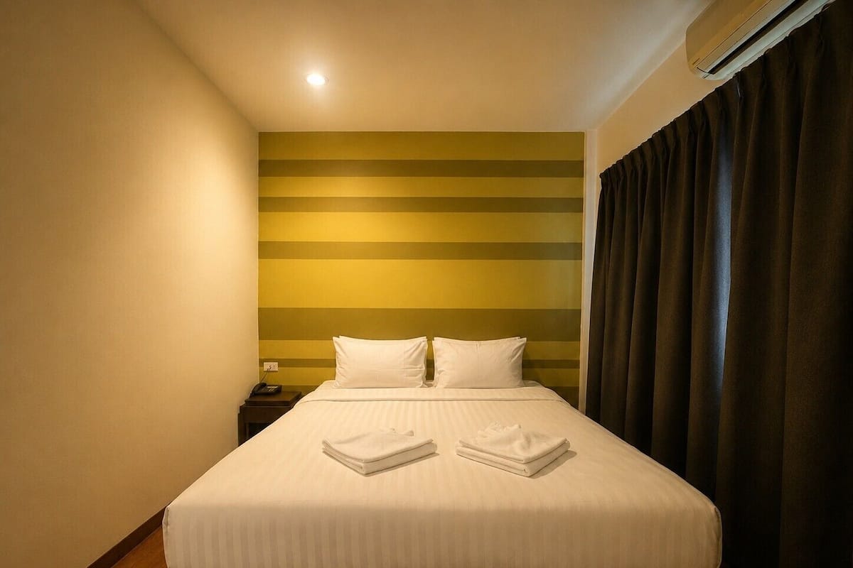 Una habitación de hotel con una cama, una mesita de noche, aire acondicionado instalado en la pared y una cortina.
