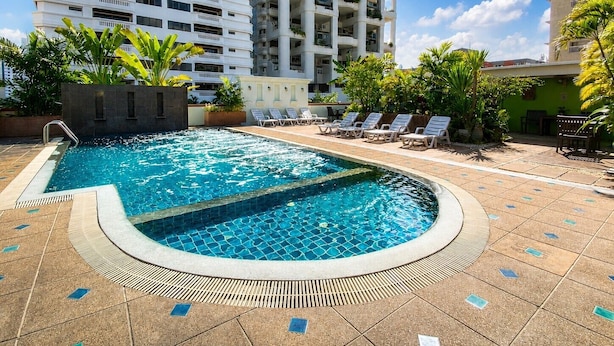 A swimming pool with lounge chairs, surrounded by greenery and modern buildings.