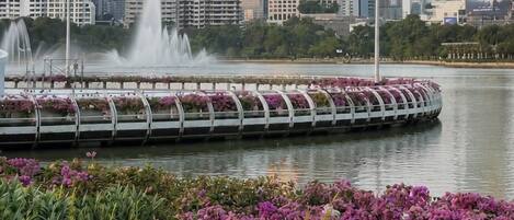 Un parque frente al agua con un paseo decorado con flores, una fuente y un horizonte urbano al fondo.