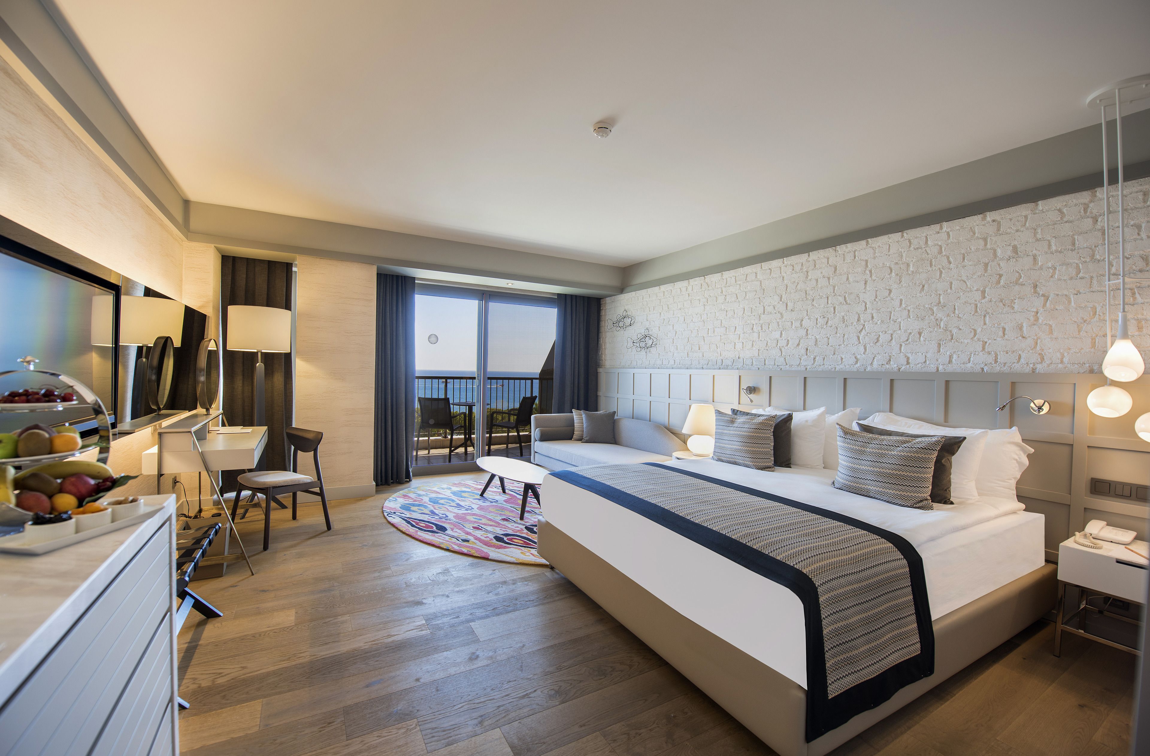A modern hotel room with a large bed, a dining area, and a view of the outdoors.