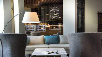 A modern lounge area with a sofa, a coffee table with a book and glasses, and a bar in the background.