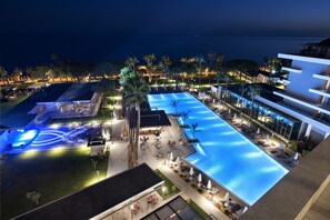 A resort with a large swimming pool, outdoor seating areas, and a view of the ocean.