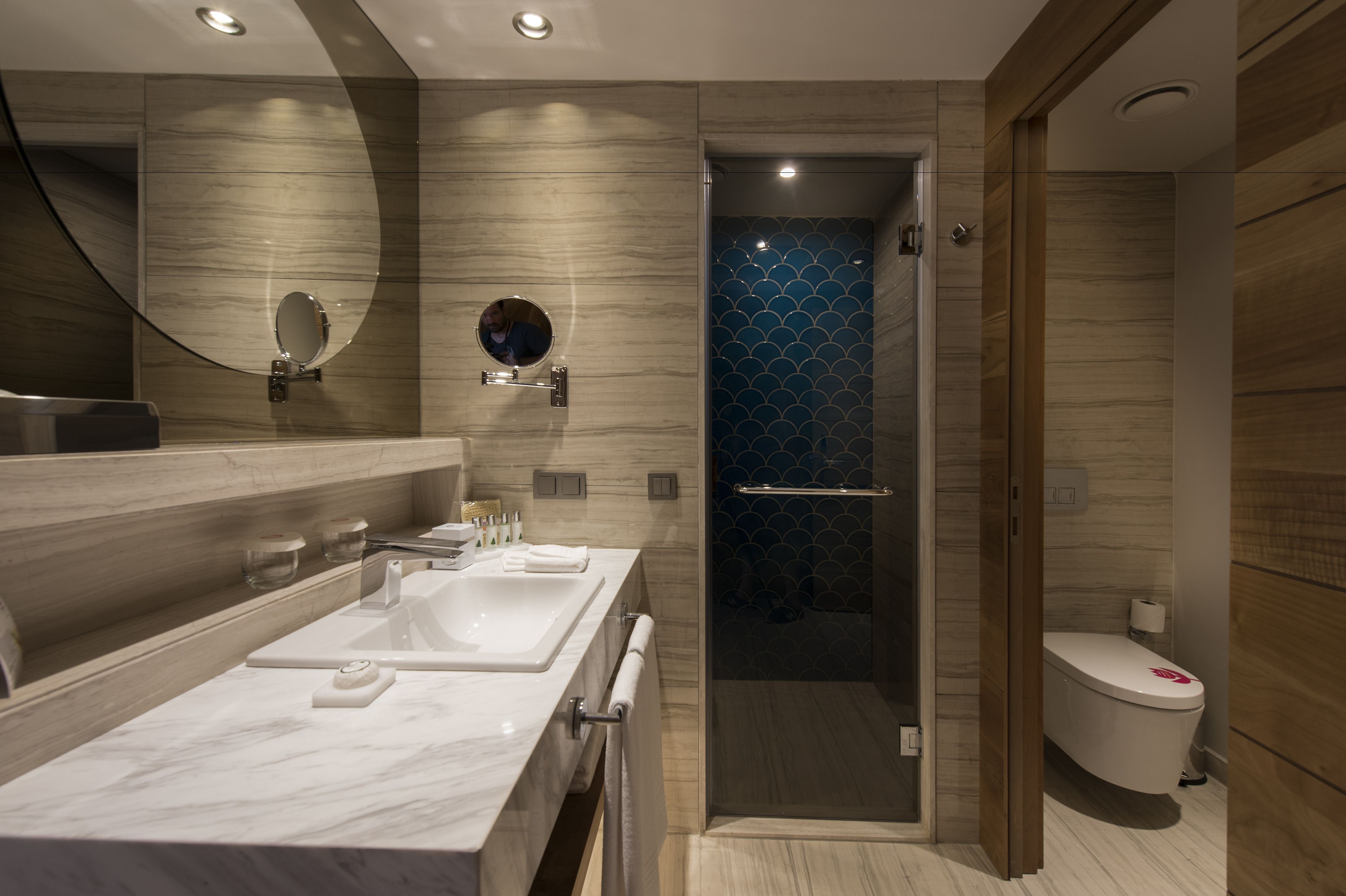 A modern bathroom with a marble vanity, a glass-enclosed shower, and a toilet with a decorative cover.