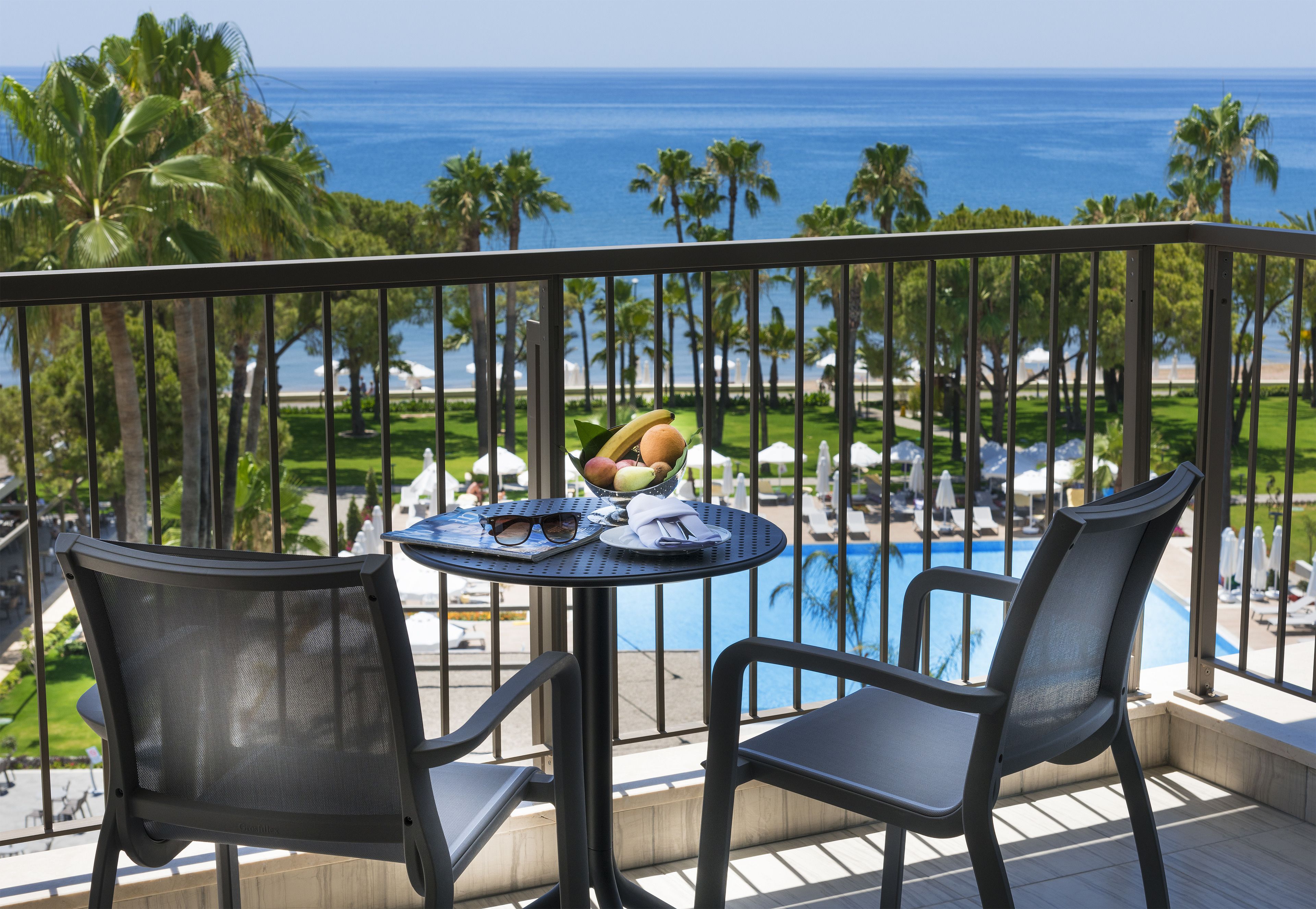 Un balcon avec deux chaises et une table, donnant sur une piscine et des palmiers.