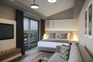 Una habitación de hotel moderna con una cama grande, un sofá, un televisor y un balcón con vistas a la ciudad.