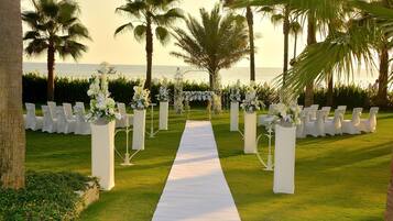 A wedding aisle with white chairs and floral arrangements, leading to a view of the ocean.