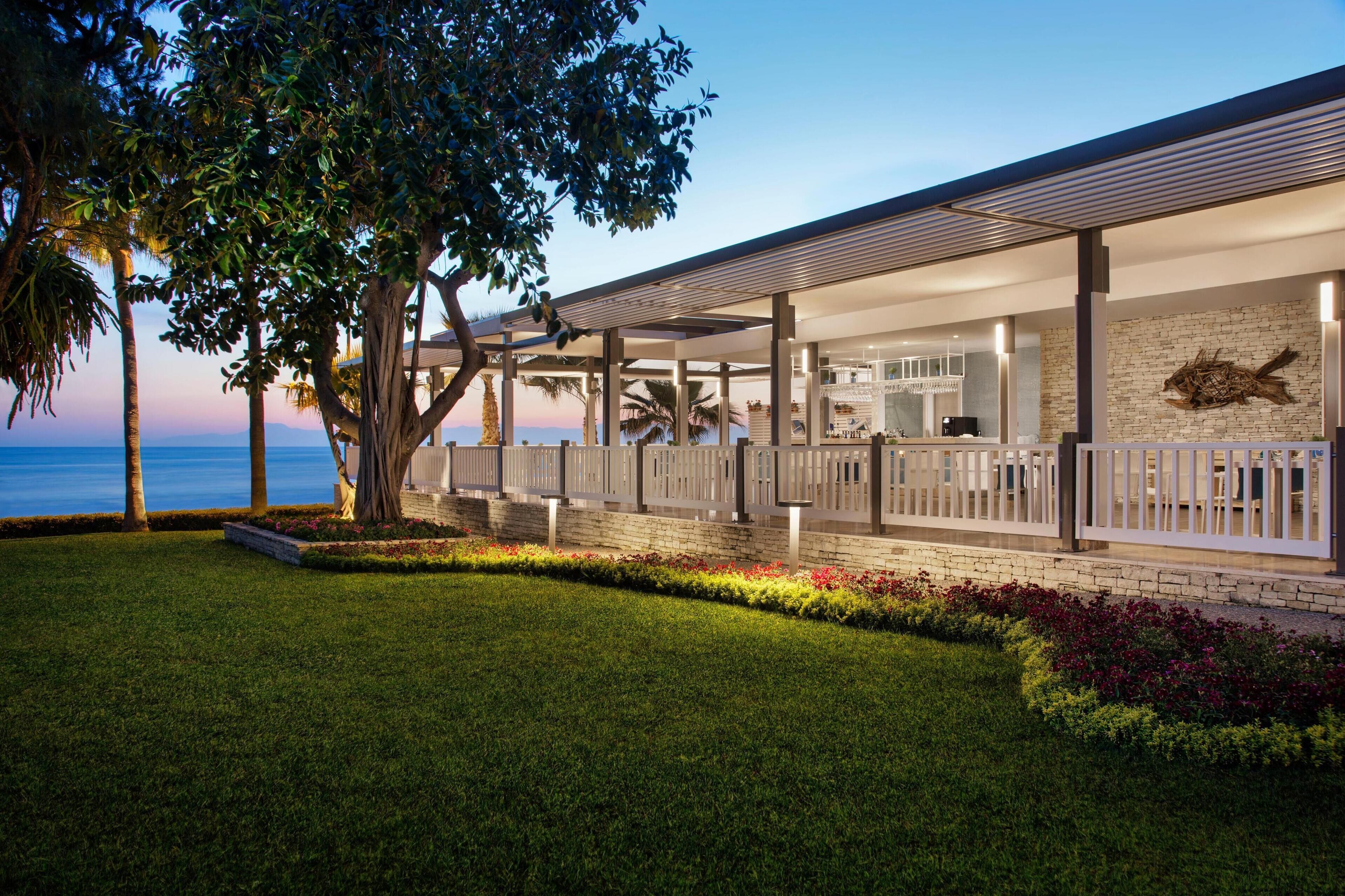 Um hotel moderno com área externa coberta, parede de pedra com escultura de peixe e vista para o oceano.