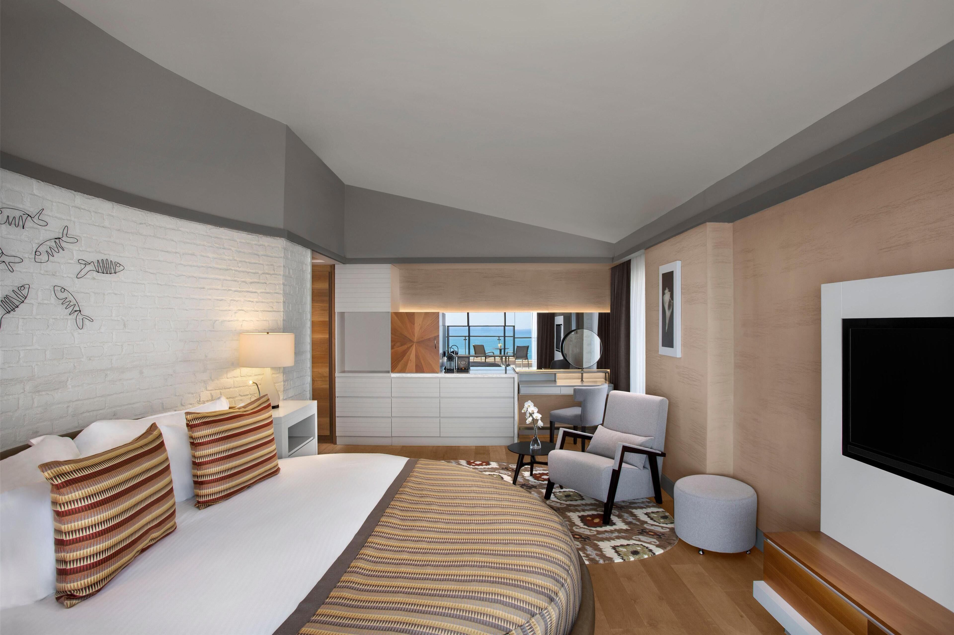 A modern hotel room with a large bed, a desk, a chair, and a TV.