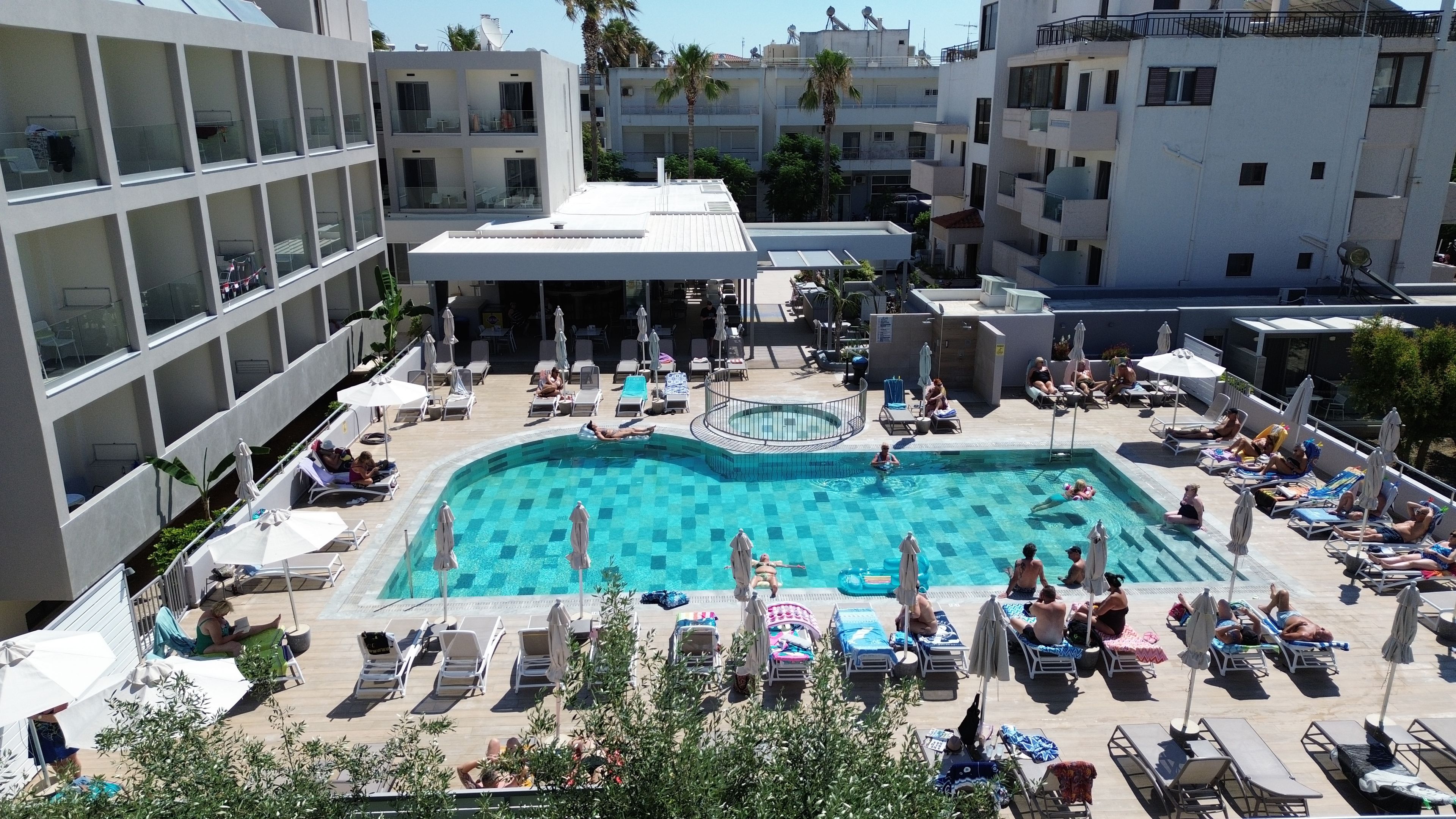 Un espace piscine aménagé sur le toit, avec des chaises longues et des parasols, entouré d’immeubles.
