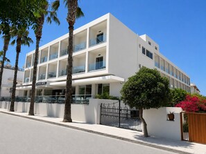 A multi-story hotel with balconies, palm trees, and a gated entrance.