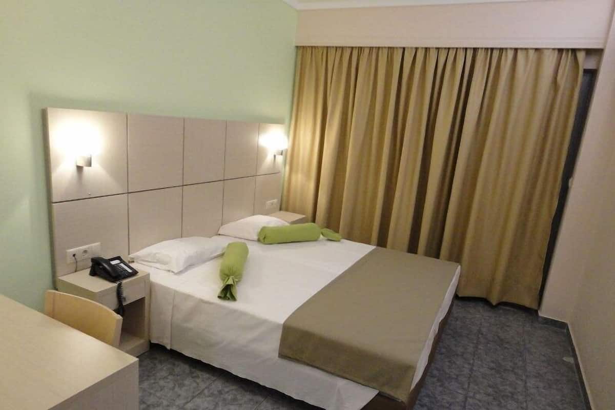 A hotel room with a bed, a bedside table with a phone, a chair, and a curtain.