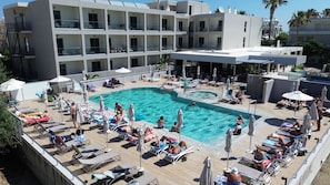 A hotel with a swimming pool surrounded by sun loungers and umbrellas, a multi-story building with balconies, and a clear sky. - Imperial Hotel (Kos)