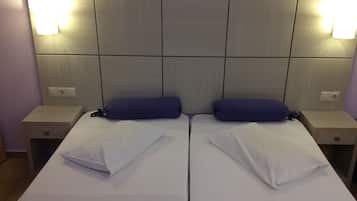A double bed with white linens and two blue pillows, flanked by nightstands with lamps, in a room with a tiled headboard.
