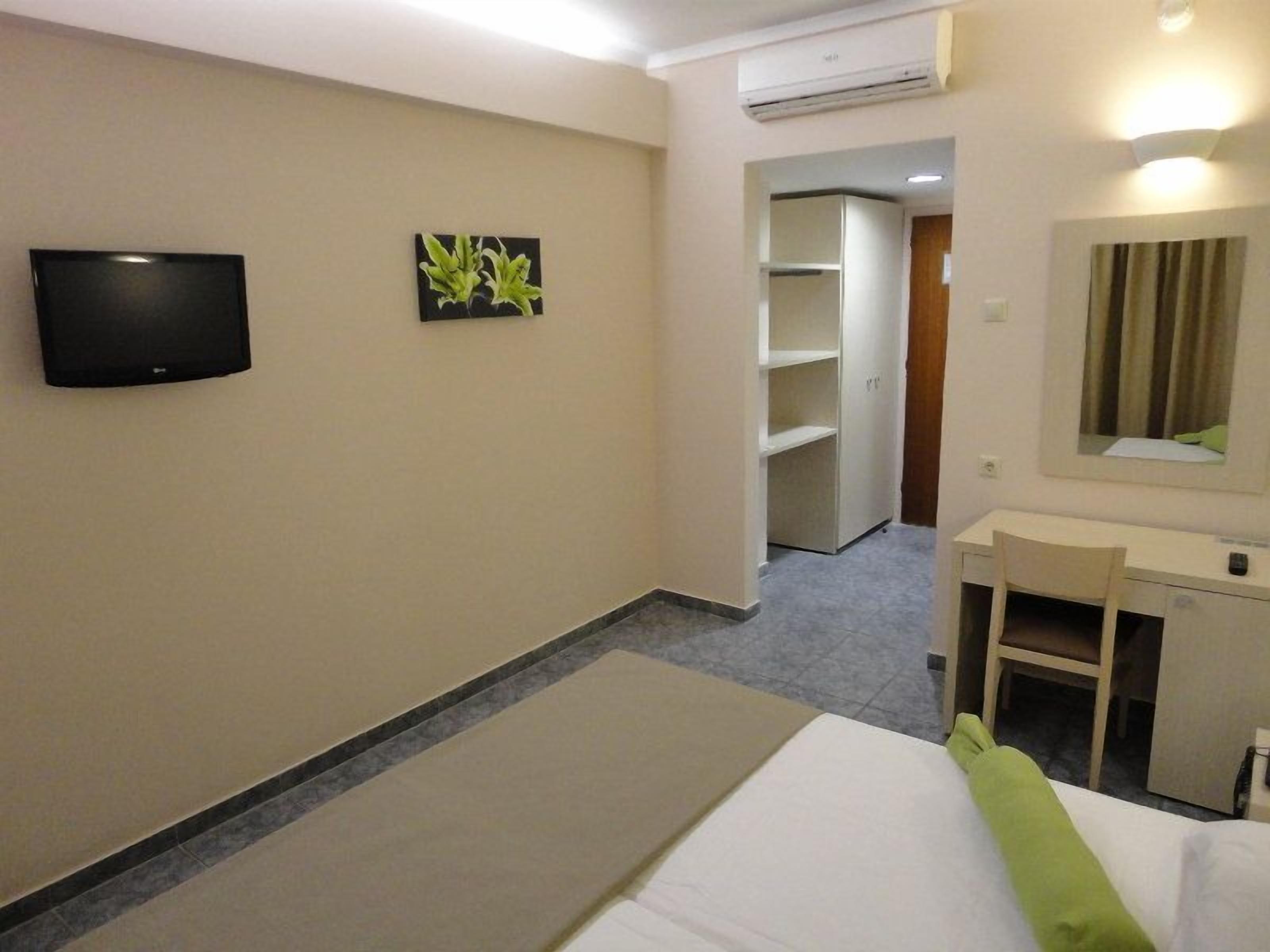 Habitación de hotel con cama, escritorio, silla, televisión, espejo y armario.