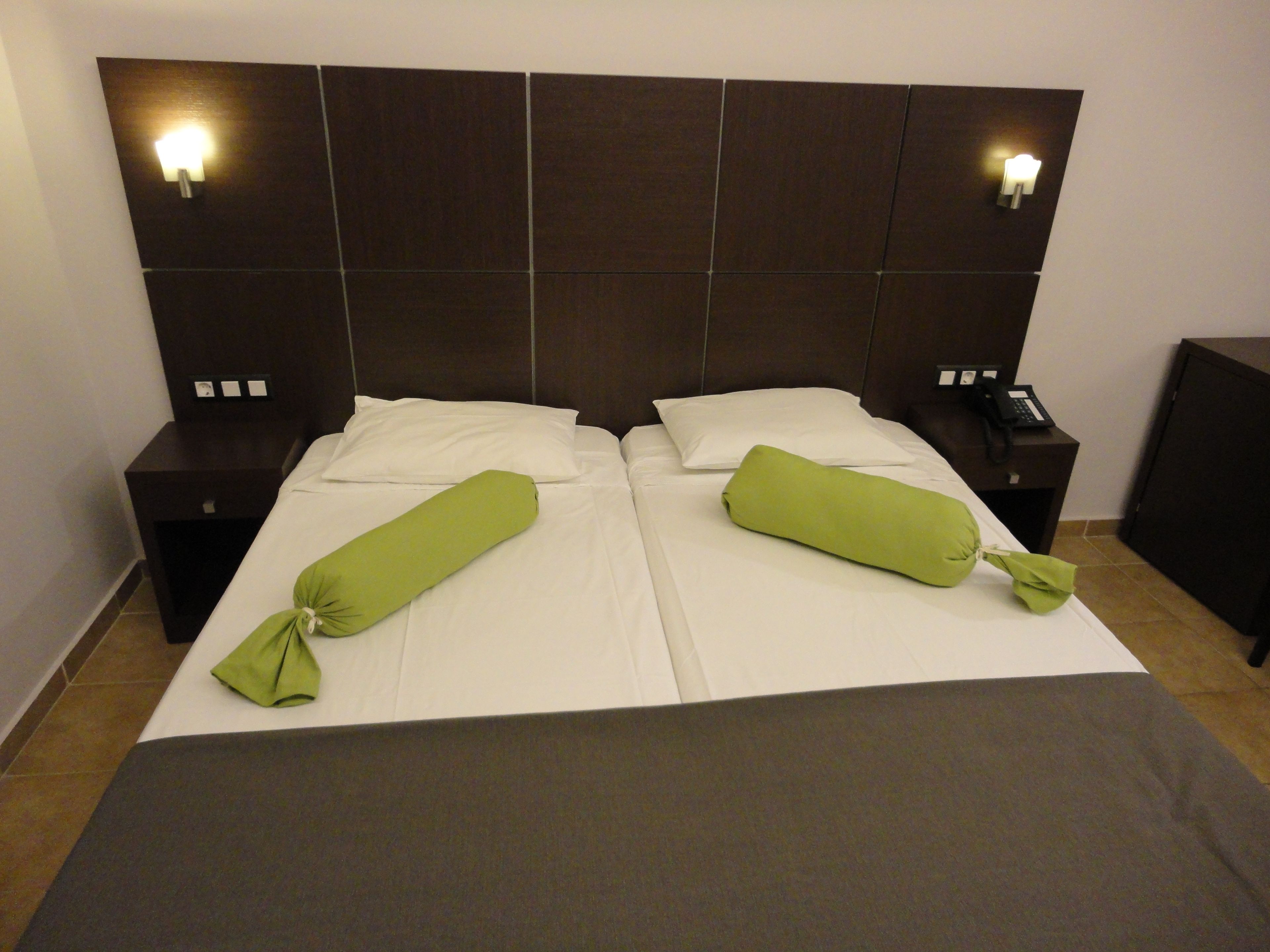 Cama doble con dos almohadas, mesita de noche con teléfono e iluminación en la pared.