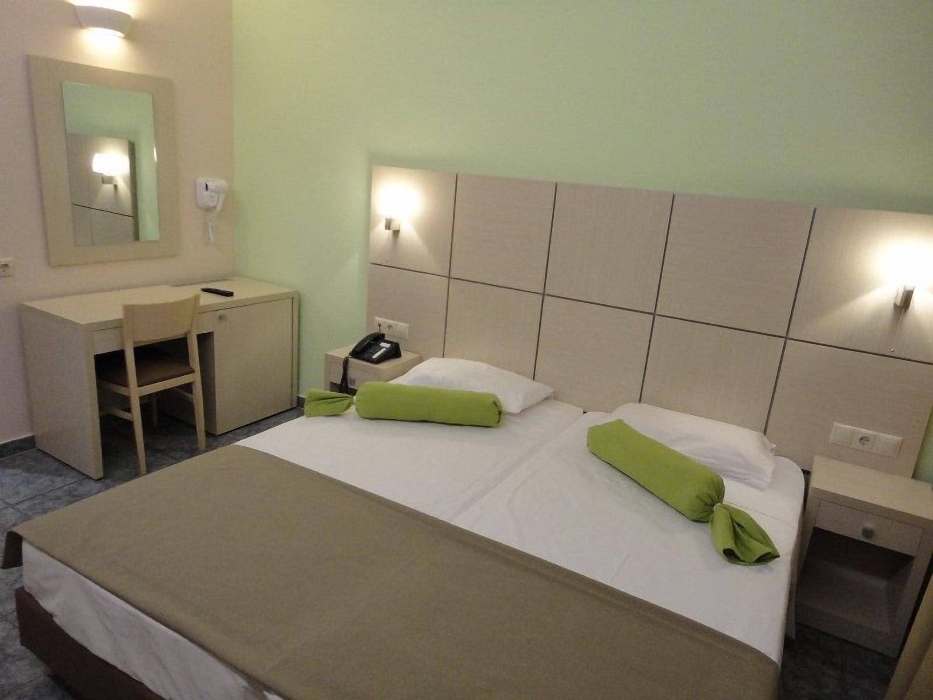 Una habitación de hotel con cama, mesita de noche, lámpara, escritorio, silla y espejo.