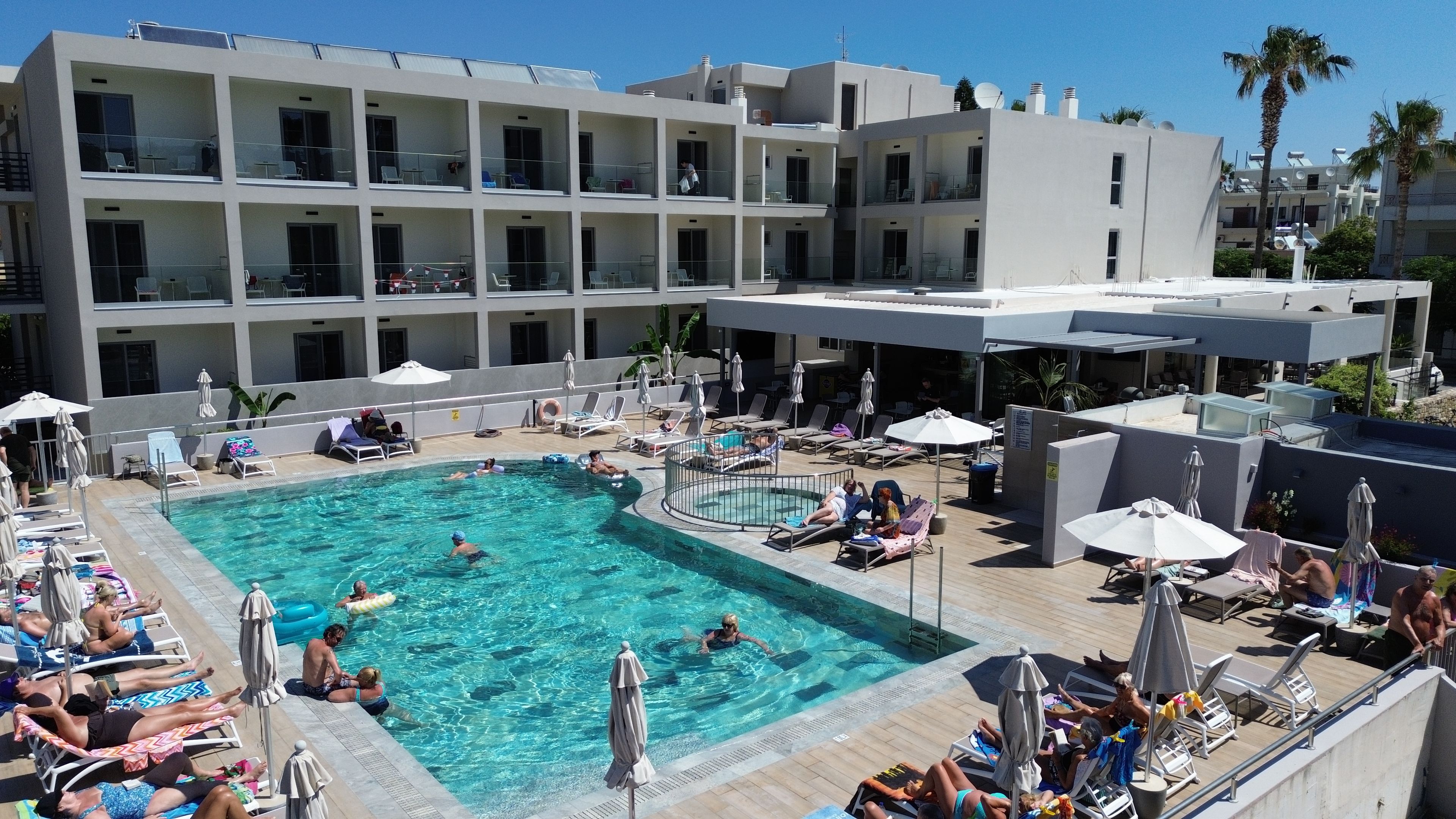 Un espace piscine d’hôtel doté de plusieurs niveaux de balcons, de chaises longues et de parasols.