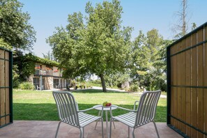 An outdoor patio with two white metal chairs and a small round table, surrounded by a wooden fence and a grassy lawn.