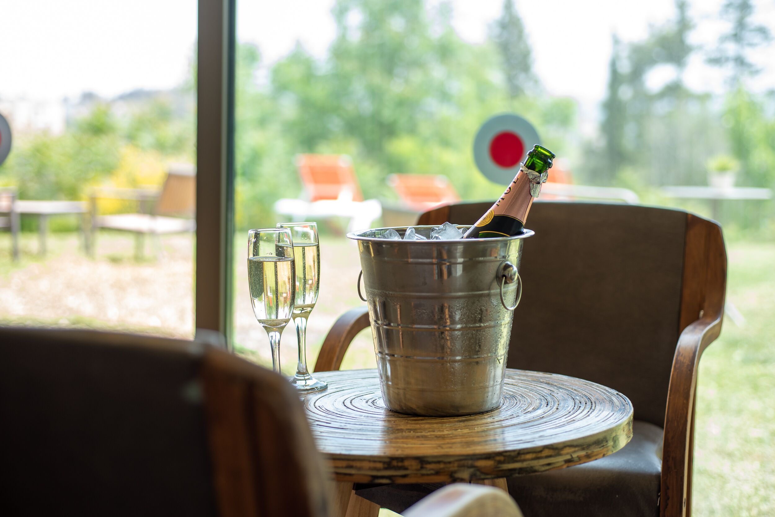 A metal bucket with a bottle of champagne and a glass on a wooden table.