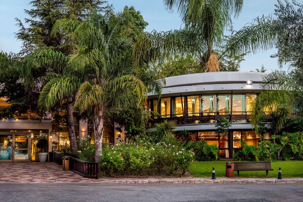 A modern building with a curved facade, surrounded by lush greenery and a well-maintained garden.