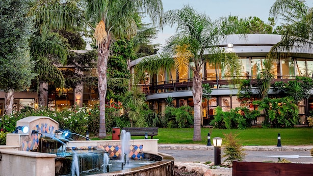 Un hôtel doté d’une fontaine, d’une végétation luxuriante et d’un bâtiment moderne avec des balcons.