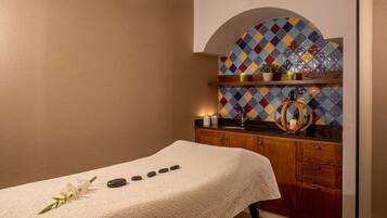 A spa room with a massage table, a wooden cabinet, and a colorful mosaic wall.