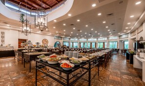 A spacious banquet hall with high ceilings, large windows, and a variety of food and drink stations.