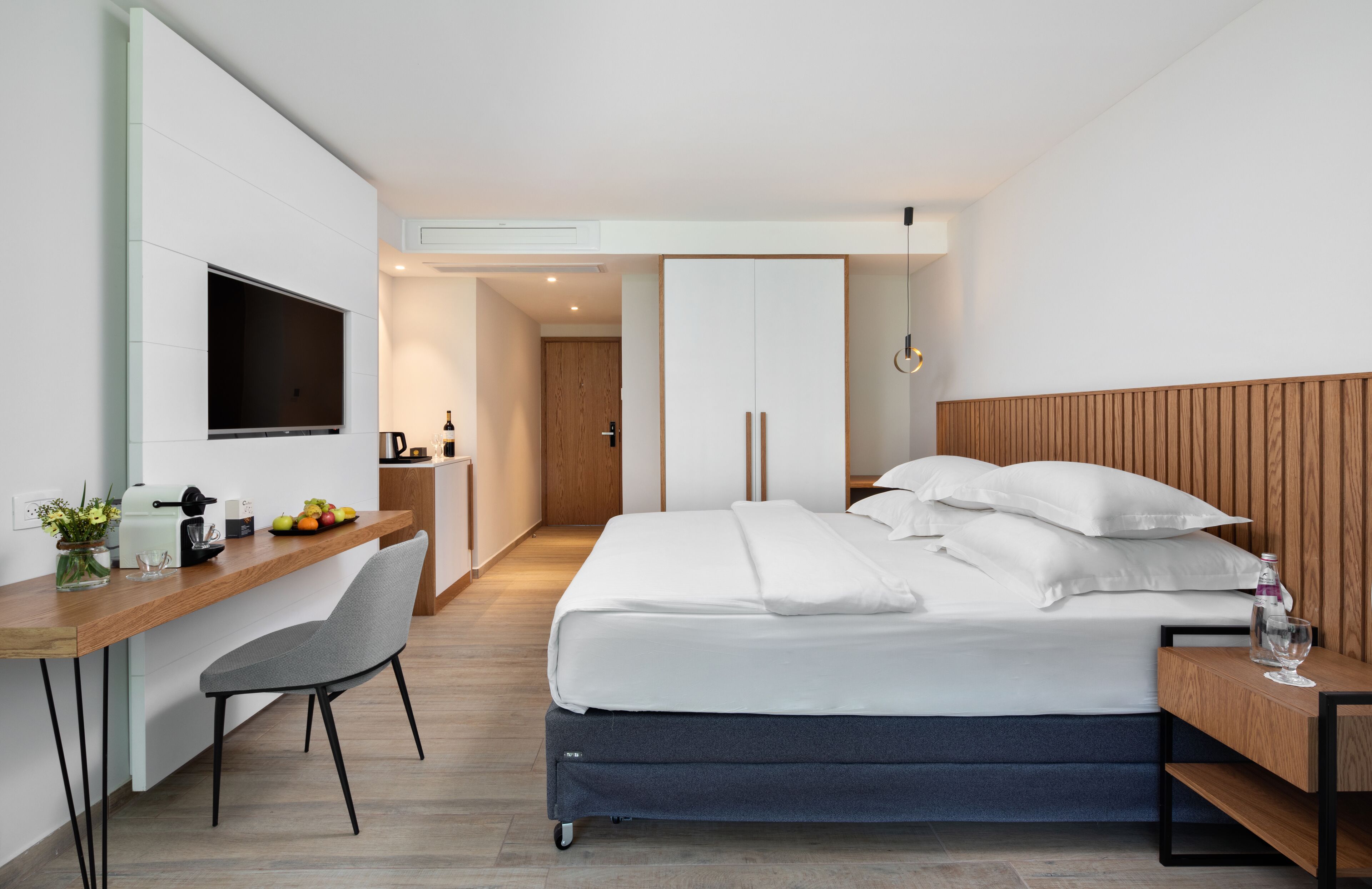 A modern hotel room with a bed, desk, chair, and a TV mounted on the wall.